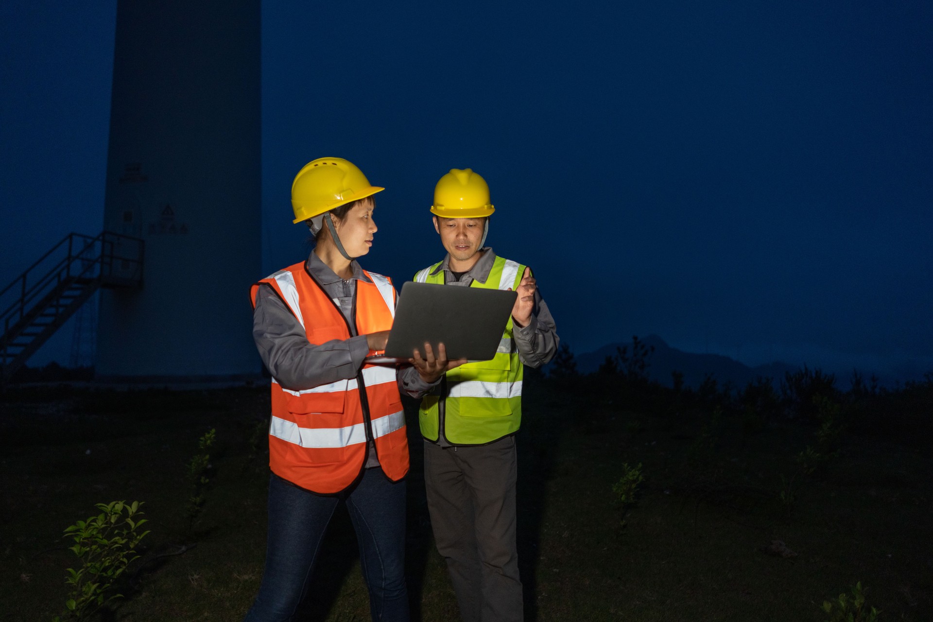 Zwei asiatische Ingenieure in der Nachtschicht arbeiten mit Computern unter der Windkraftanlage